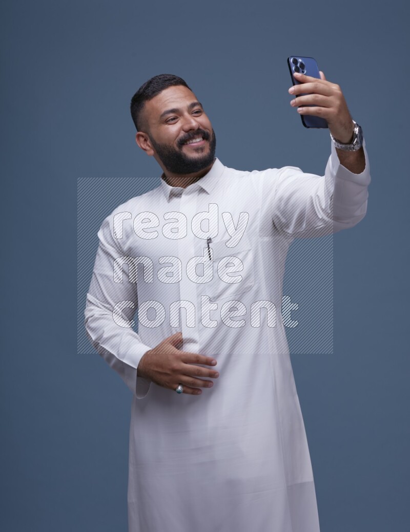 A Saudi man Taking A Selfie on Blue Background wearing Saudi Thob