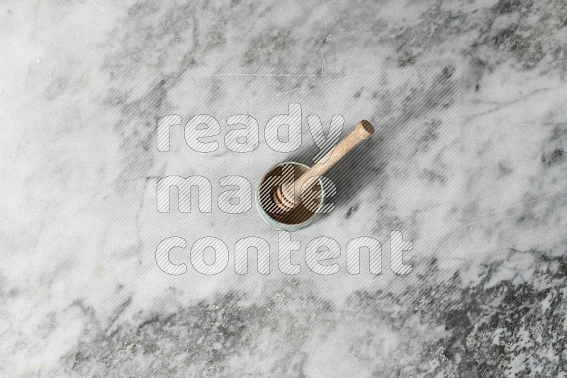 Multicolored Pottery Bowl with wooden honey handle in it, on grey marble flooring, Top View