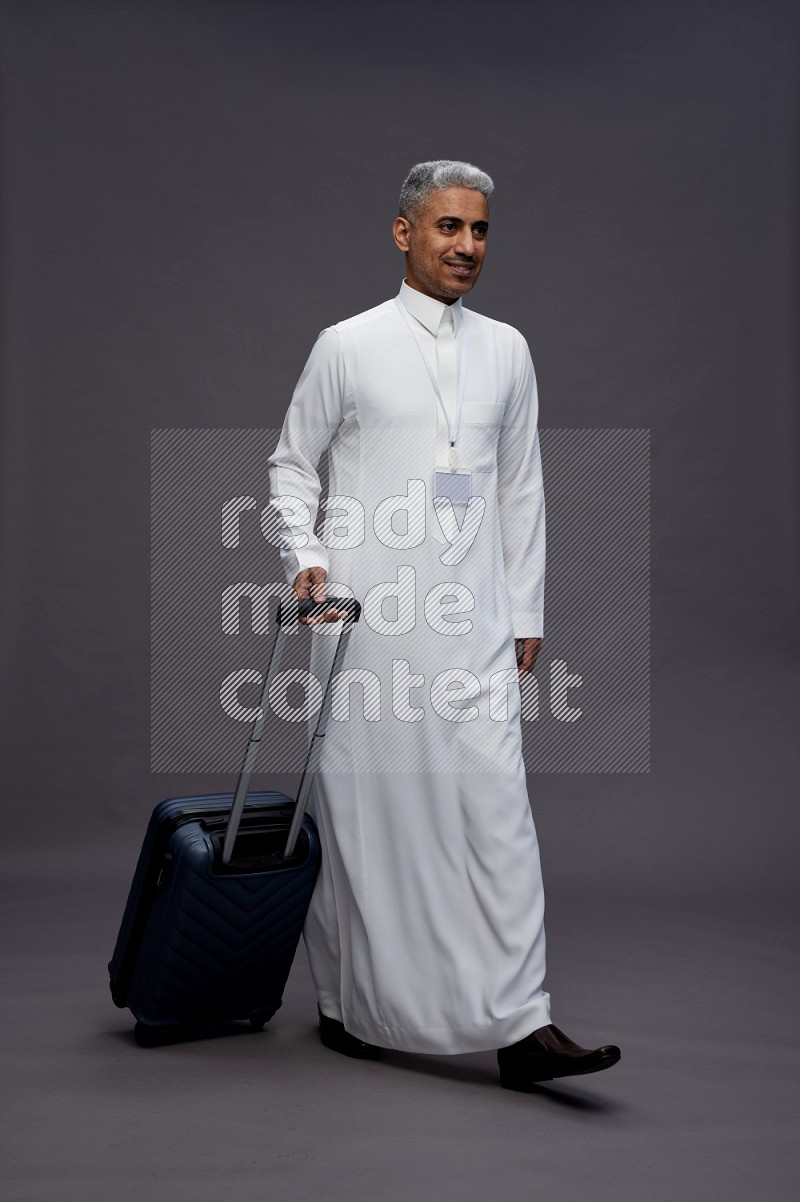 Saudi man wearing thob with neck strap employee badge standing holding bag on gray background