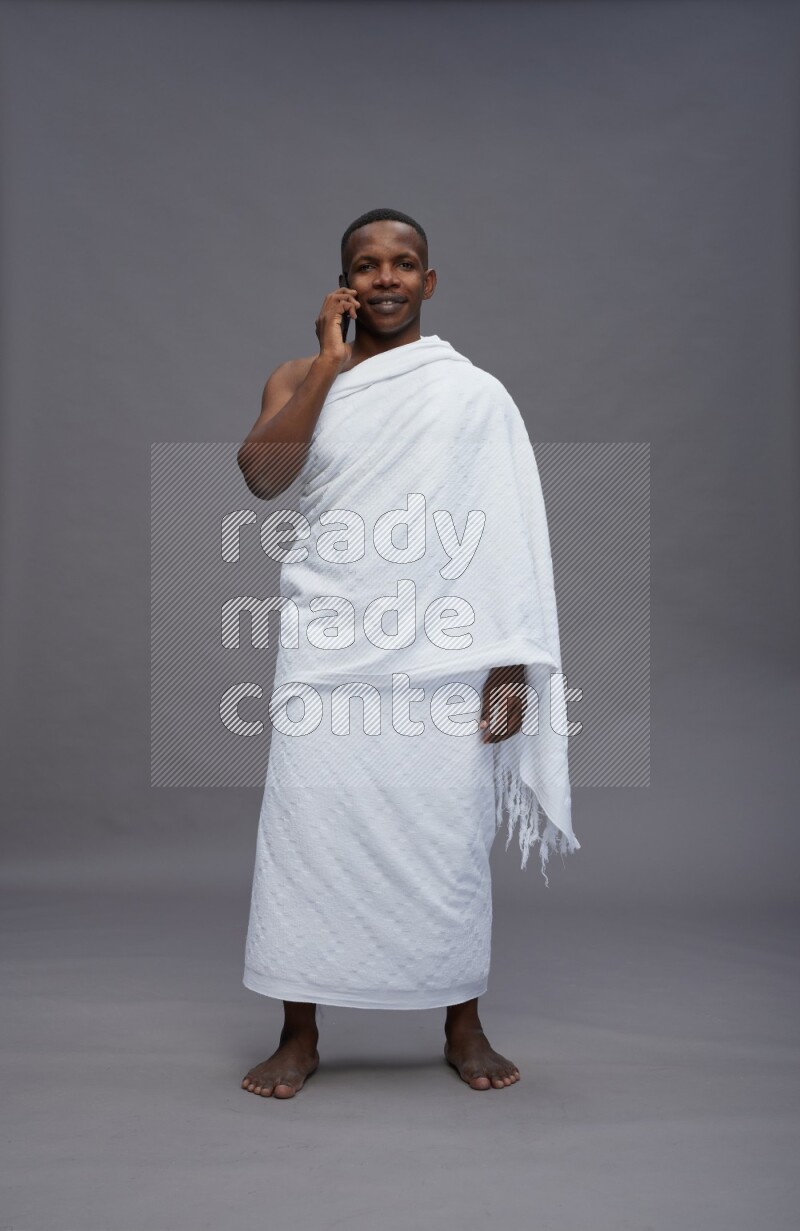 A man wearing Ehram Standing talking on phone on gray background