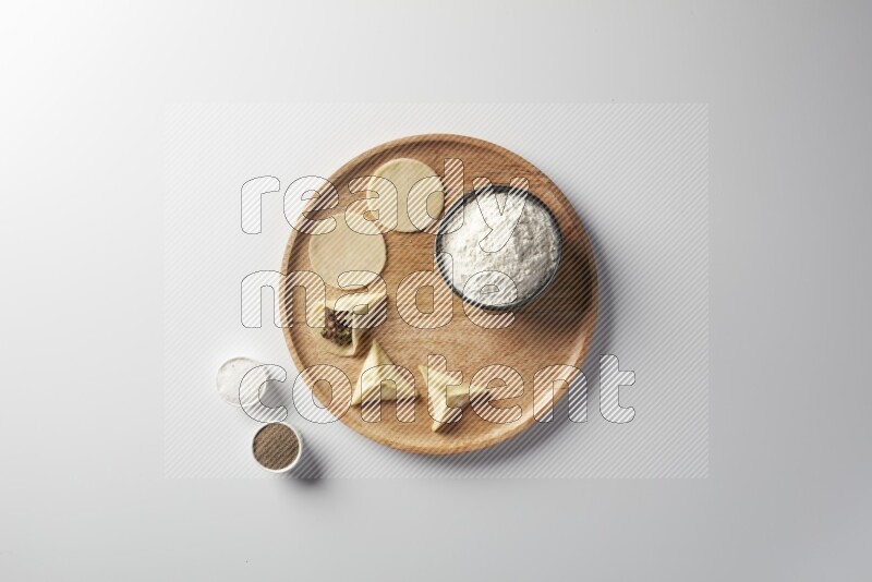 two closed sambosas and one open sambosa filled with meat while flour, salt, and black pepper aside in a wooden dish on a white background