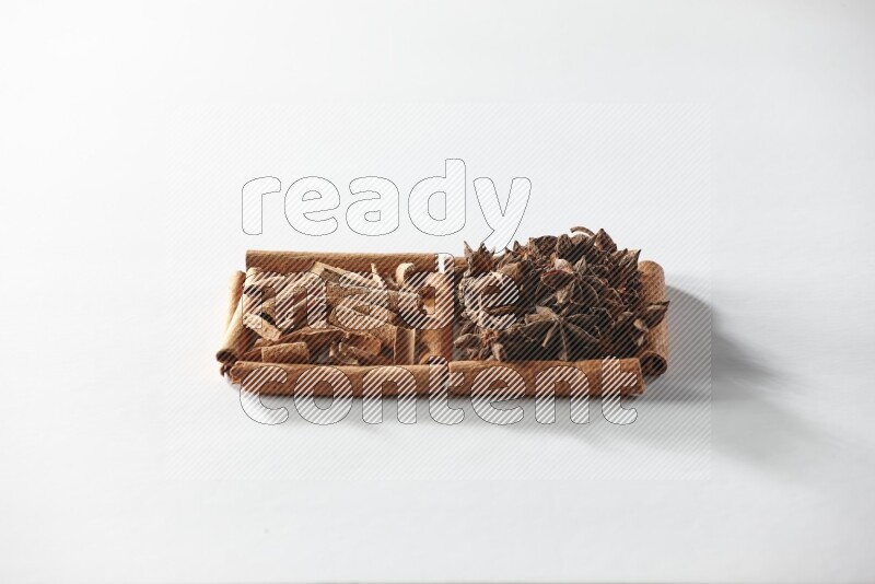 مربعان من أعواد القرفة ممتلئان باليانسون النجمي وقطع من القرفة علي خلفية بيضاء