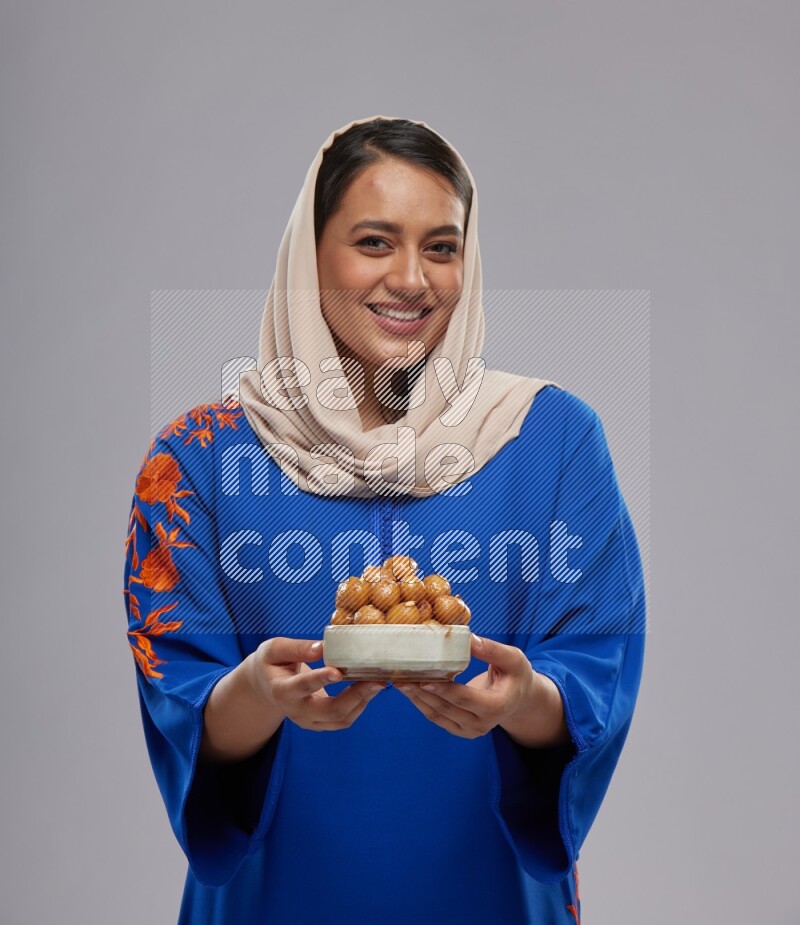 A Saudi woman standing wearing Jalabeya holding a plate of luqaimat