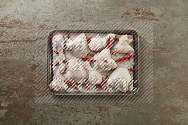 Mixed fresh chicken pieces in an oven tray on a textured rustic background