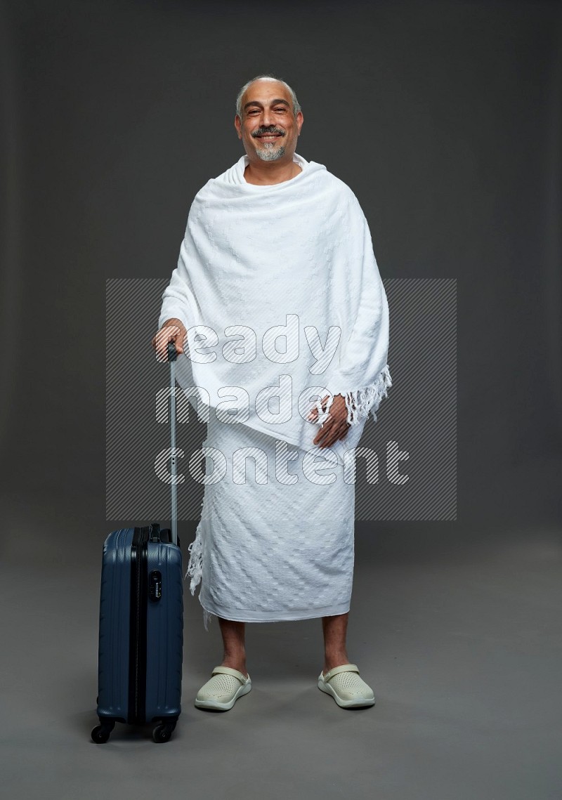 A man wearing Ehram Standing holding traveling bag on gray background