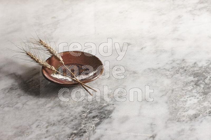 Wheat stalks on decorative pottery plate on grey marble background