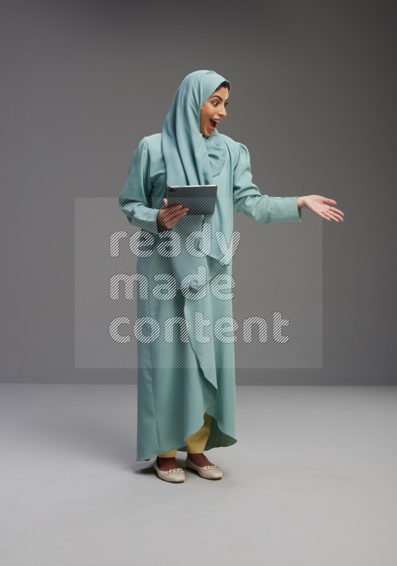 Saudi Woman wearing Abaya standing working on tablet on Gray background