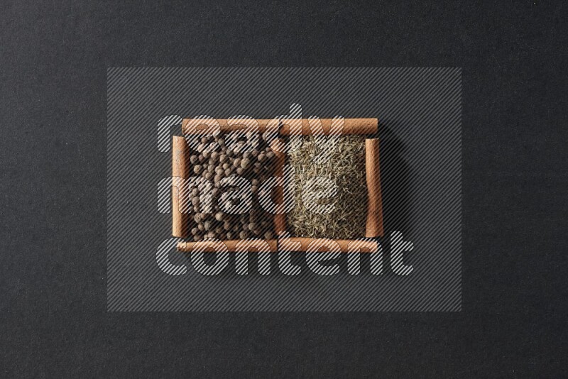 مربعان من أعواد القرفة ممتلئان بحبوب الكمون وحبوب بهار الفلفل الحلو علي خلفية سوداء