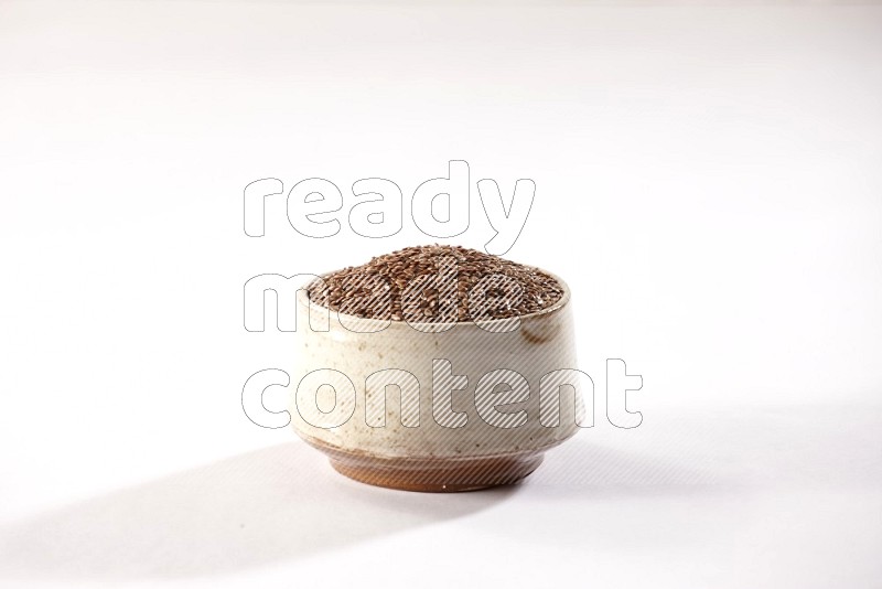 A pottery beige bowl full of flax seeds on a white flooring