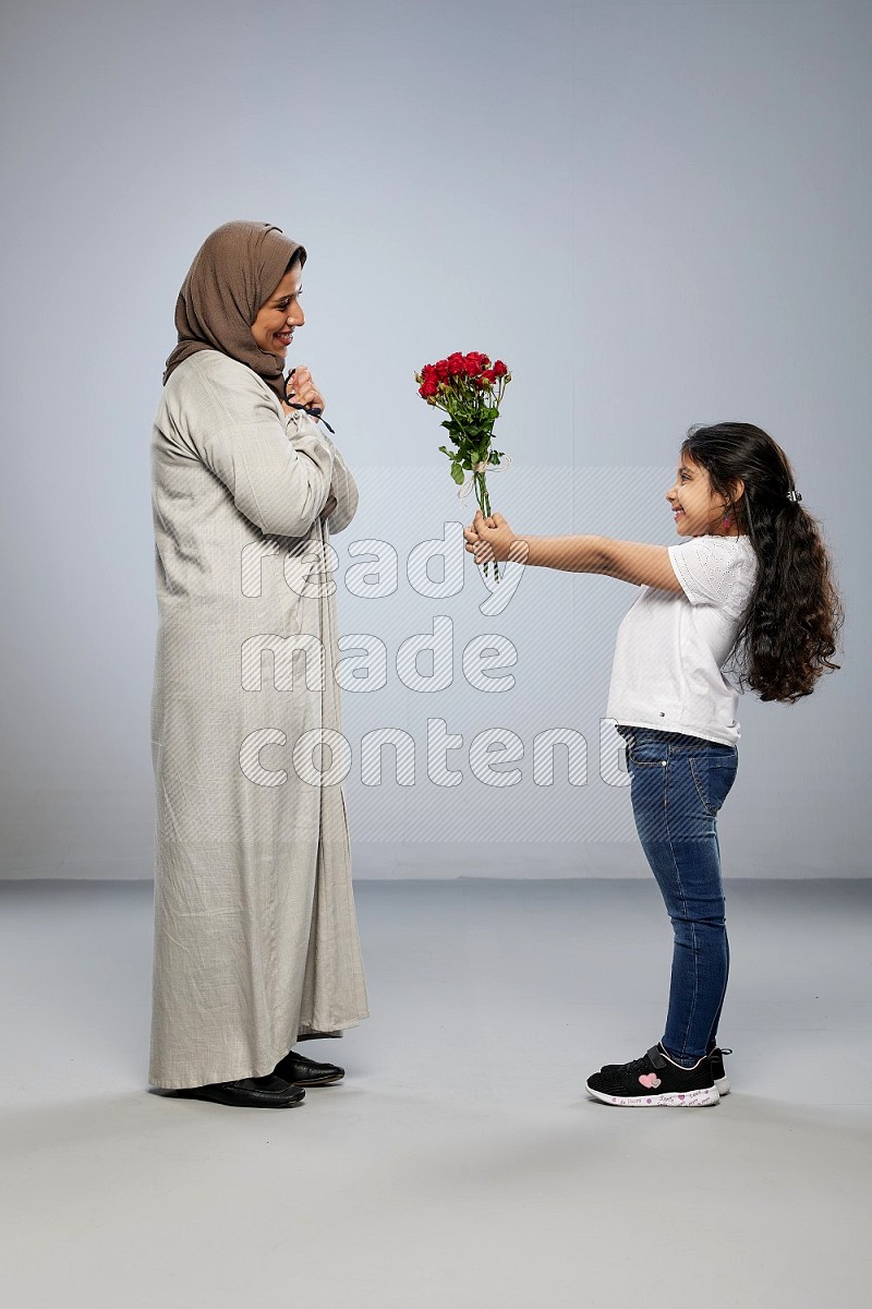 A girl standing giving flowers to her mother on gray background