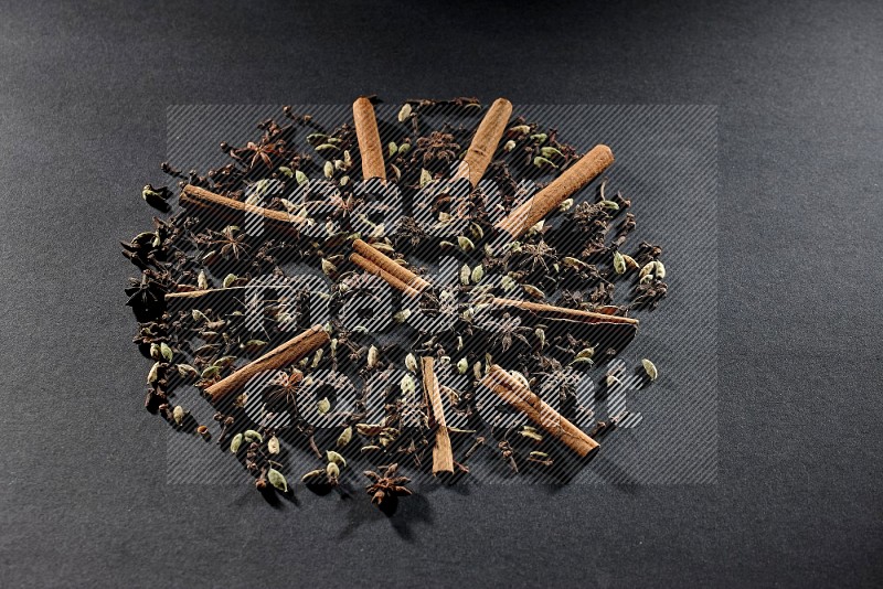 Cardamom, star anise, cloves and cinnamon sticks on black flooring