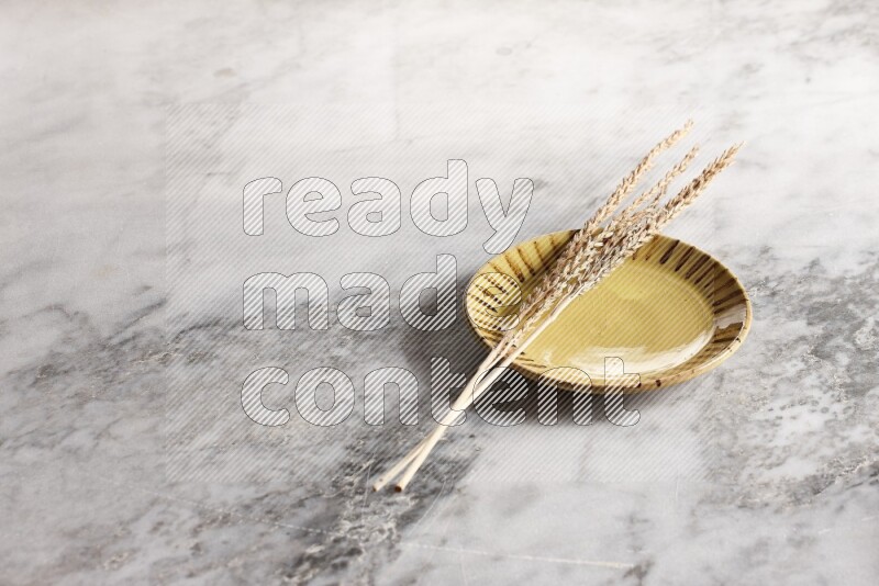 Wheat stalks on multicolored pottery plate on grey marble background