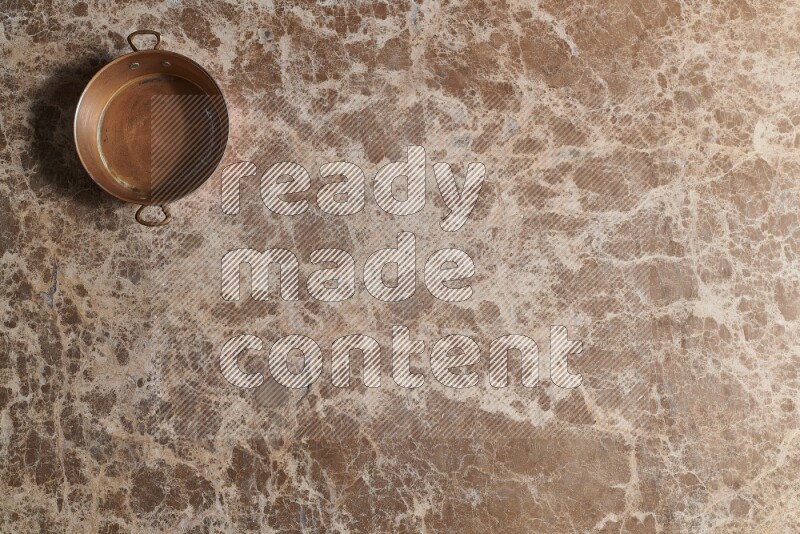 A small copper pan on beige marble background