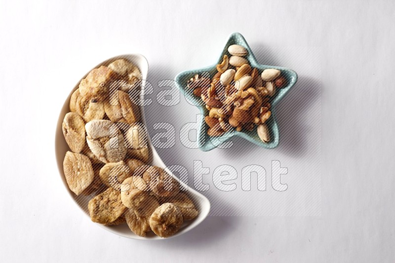 Dried figs in a crescent pottery plate and a star shaped plate with mixed nuts on white background