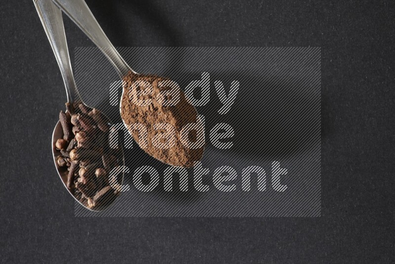 ملعقتان معدنيتان، إحداهما ممتلئة بحبوب القرنفل والأخرى ببودرة القرنفل، على خلفية سوداء