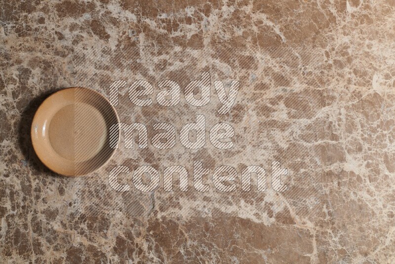 A beige pottery plate on beige marble background