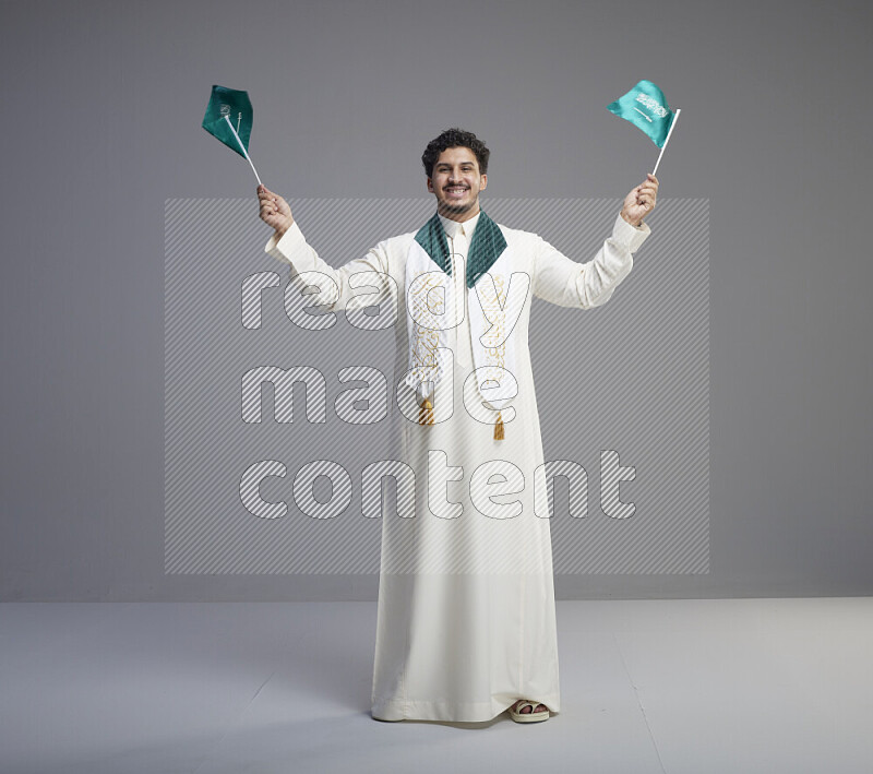 رجل سعودي يرتدي ثوب ابيض ويحمل علم السعودية