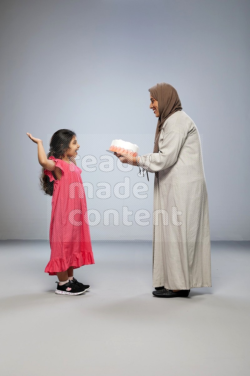 A mother giving a cake to her daughter on gray background