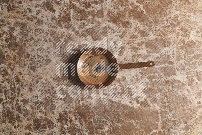 Top View Shot Of A Small Copper pan On beige Marble Flooring