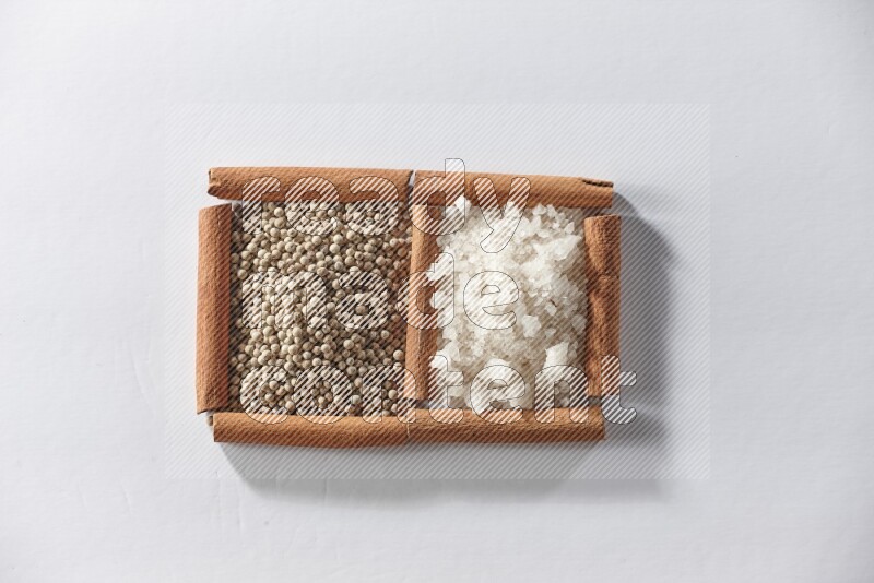 مربعان من أعواد القرفة ممتلئان بحبوب الفلفل الأبيض والملح الأبيض علي خلفية بيضاء