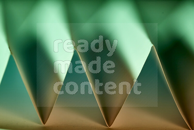 A close-up abstract image showing sharp geometric paper folds in green gradients and warm tones