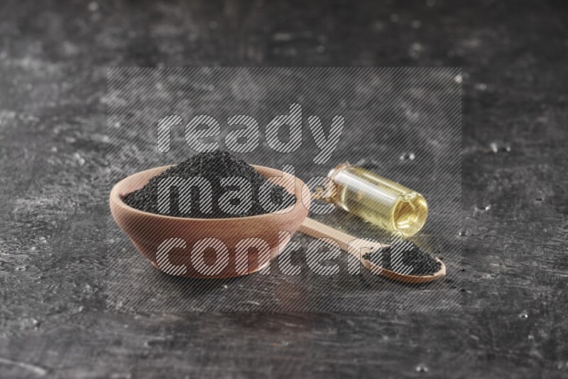 وعاء خشبي وملعقة خشبية ممتلئان ببذور حبة البركة مع زجاجة من زيت حبة البركة علي خلفية سوداء