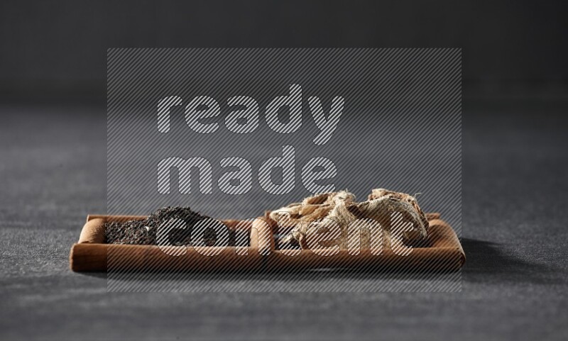 مربعان من أعواد القرفة ممتلئان بالزنجبيل المجفف والشاي الأسود علي خلفية سوداء