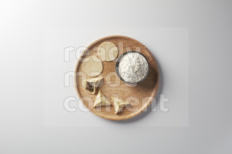 two closed sambosas and one open sambosa filled with meat while flour aside in a wooden dish on a white background