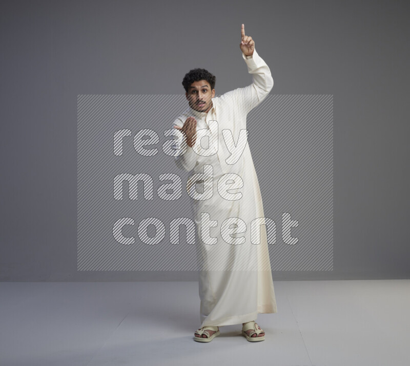 A Saudi man standing wearing thob interacting with the camera on gray background