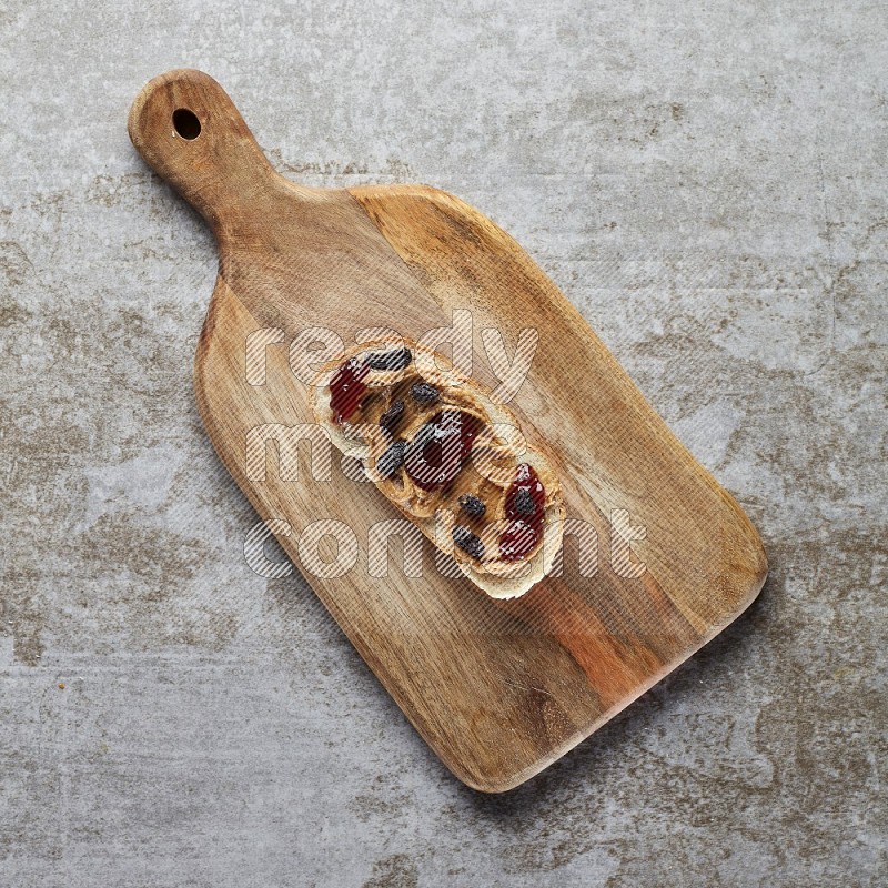 open faced peanut butter sandwich with jam and dried cranberries on a grey textured background