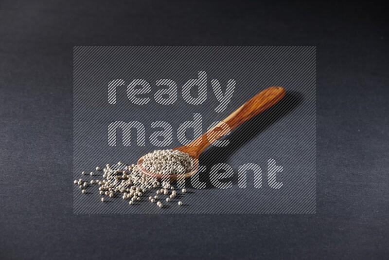 A wooden ladle full of white pepper beads on black flooring