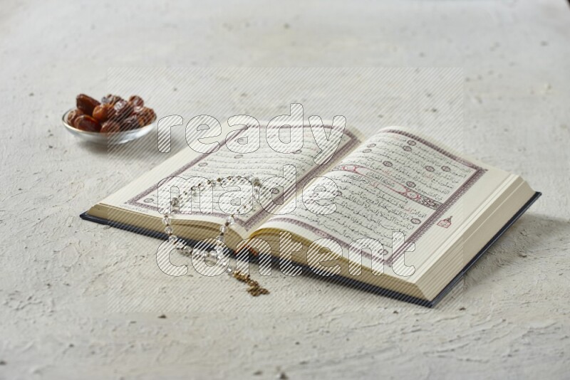 Quran with dates, prayer beads and different drinks all placed on textured white background