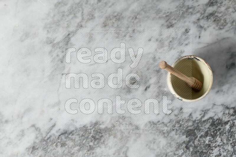 Decorative pottery bowl with wooden honey dipper in it on grey marble background
