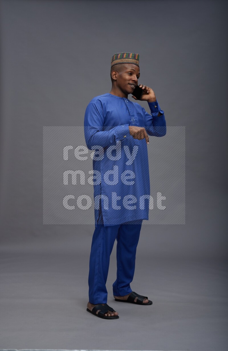 Man wearing Nigerian outfit standing talking on phone on gray background