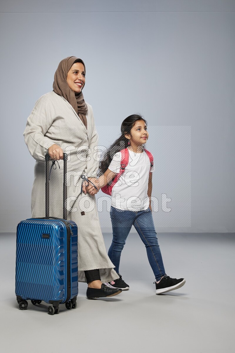 Mom and daughter standing pulling a carry-on bag on gray background