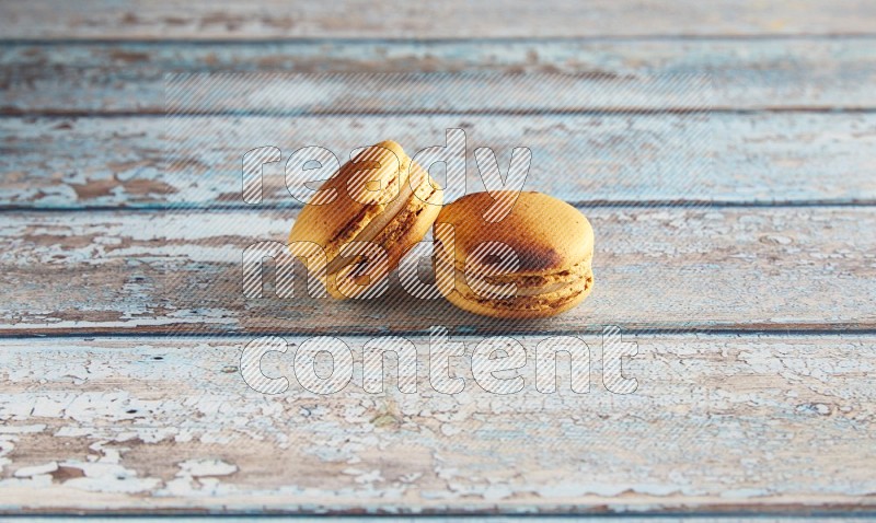 45º Shot of two Yellow Crème Brulée macarons on light blue wooden background