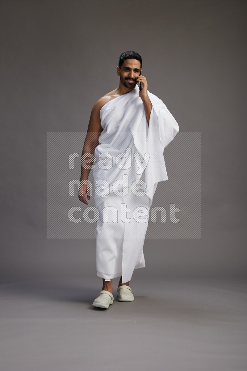 A man wearing Ehram Standing talking on phone on gray background