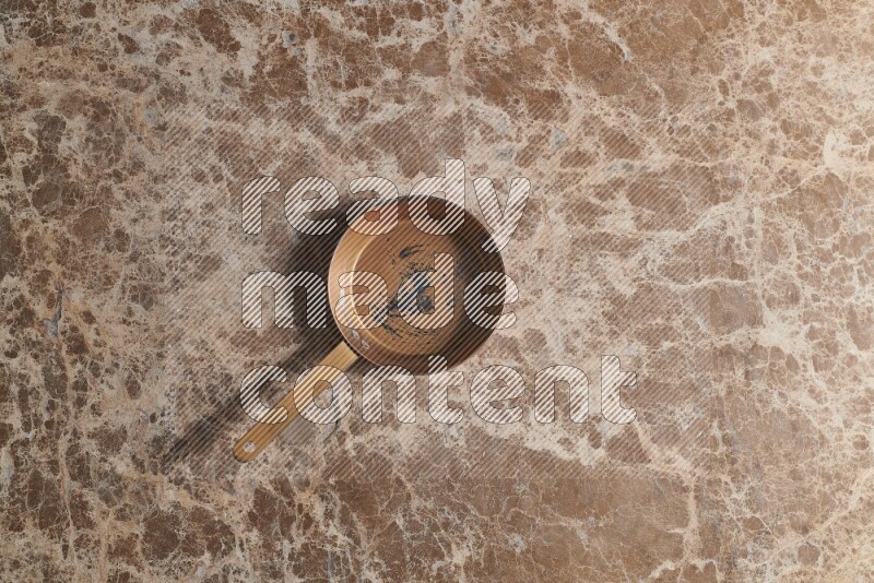 A small copper pan on beige marble background
