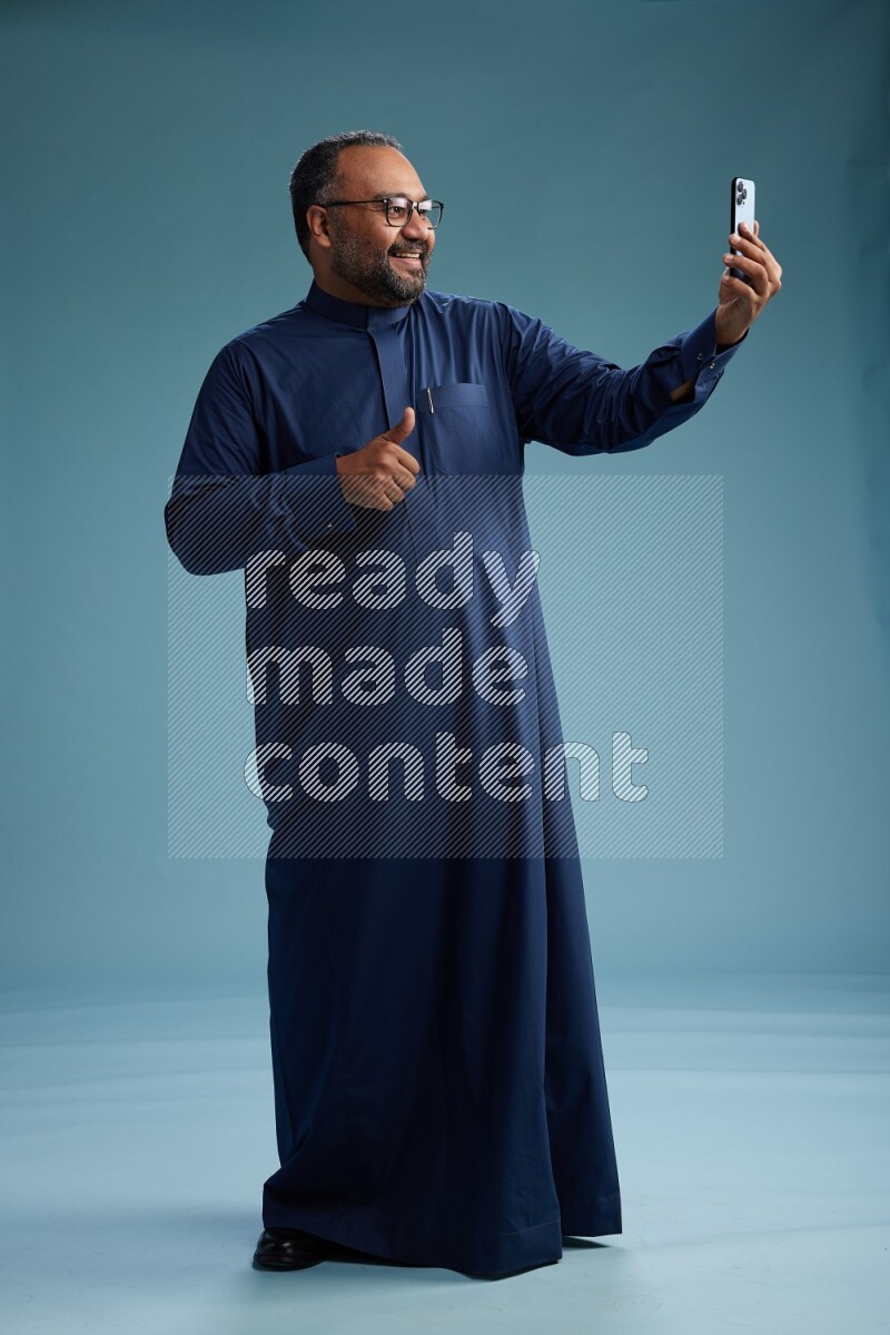 Saudi Man without shimag Standing taking selfie on blue background