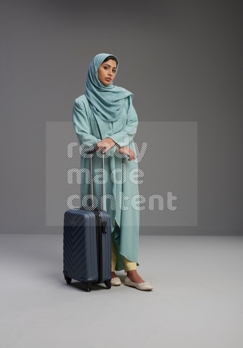 Saudi Woman wearing Abaya standing holding Travel bag on Gray background