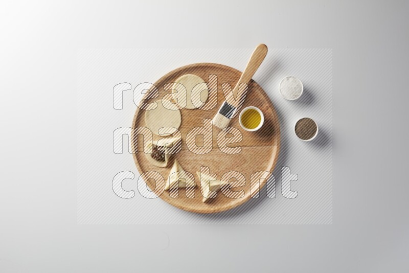 two closed sambosas and one open sambosa filled with meat while salt, black pepper and oil with oil brush aside in a wooden dish on a white background