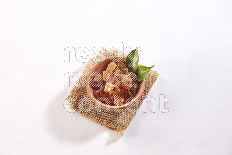 A wooden bowl full of gum arabic on a piece of burlap on white flooring in different angles