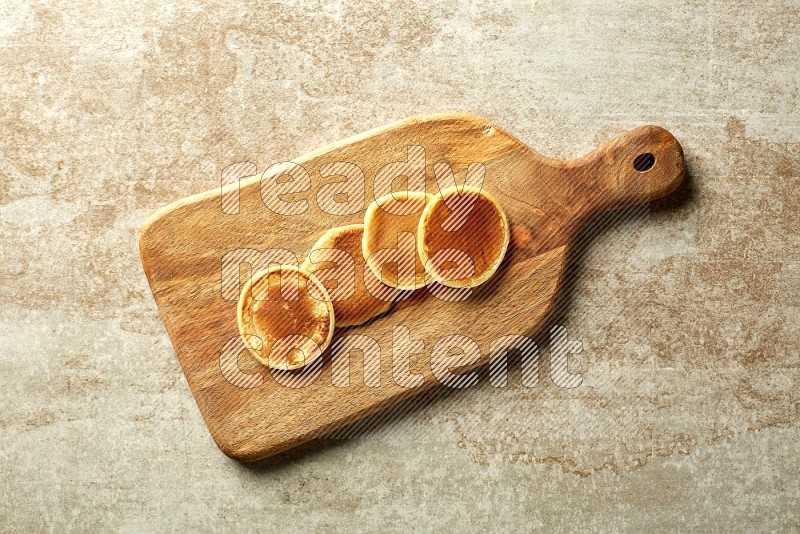 Four stacked plain mini pancakes on a wooden board on beige background
