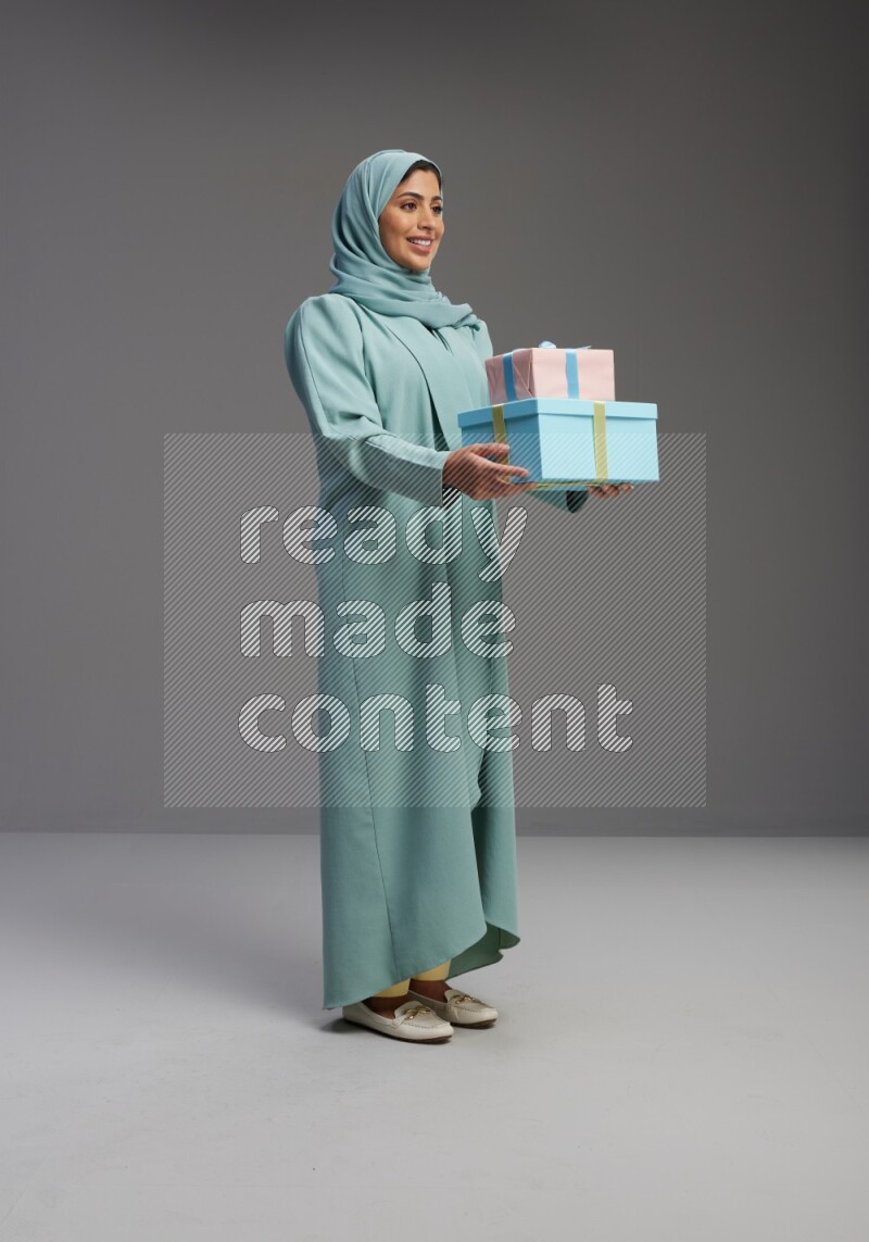 Saudi Woman wearing Abaya standing holding gift box on Gray background