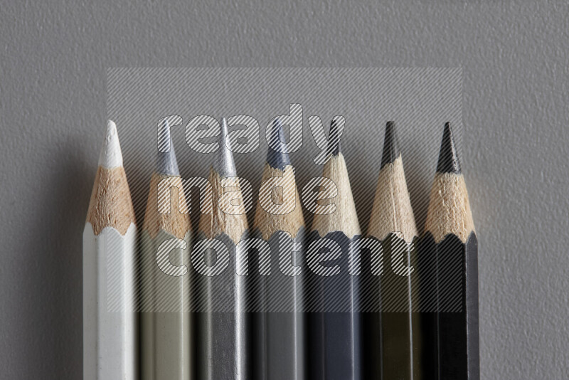 مجموعة من أقلام الرصاص الملونة مرتبة لتعرض تدرجا من اللون الأبيض والرمادي والأسود علي خلفية رمادية
