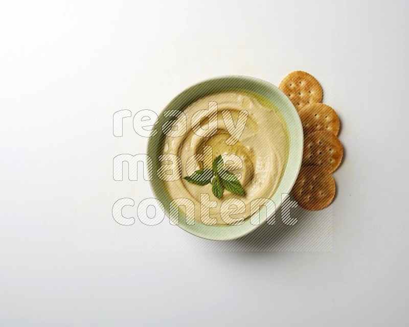 Hummus in a green plate garnished with mint on a white background