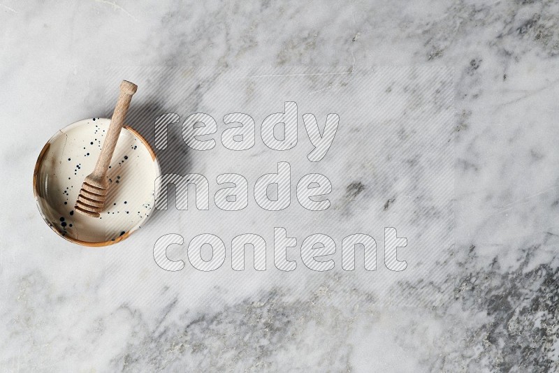 Multicolored Pottery bowl with wooden honey handle in it, on grey marble flooring, Top View