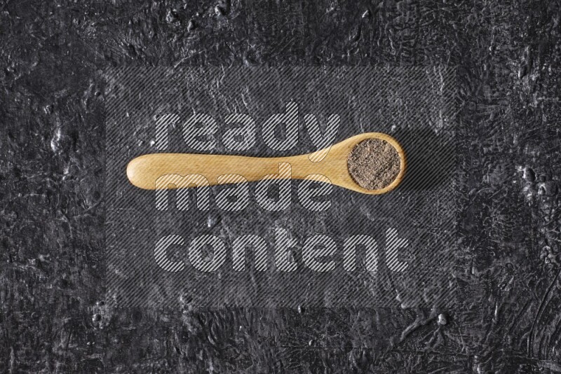 حبوب الفلفل الأسود في ملعقة خشبية علي خلفية سوداء