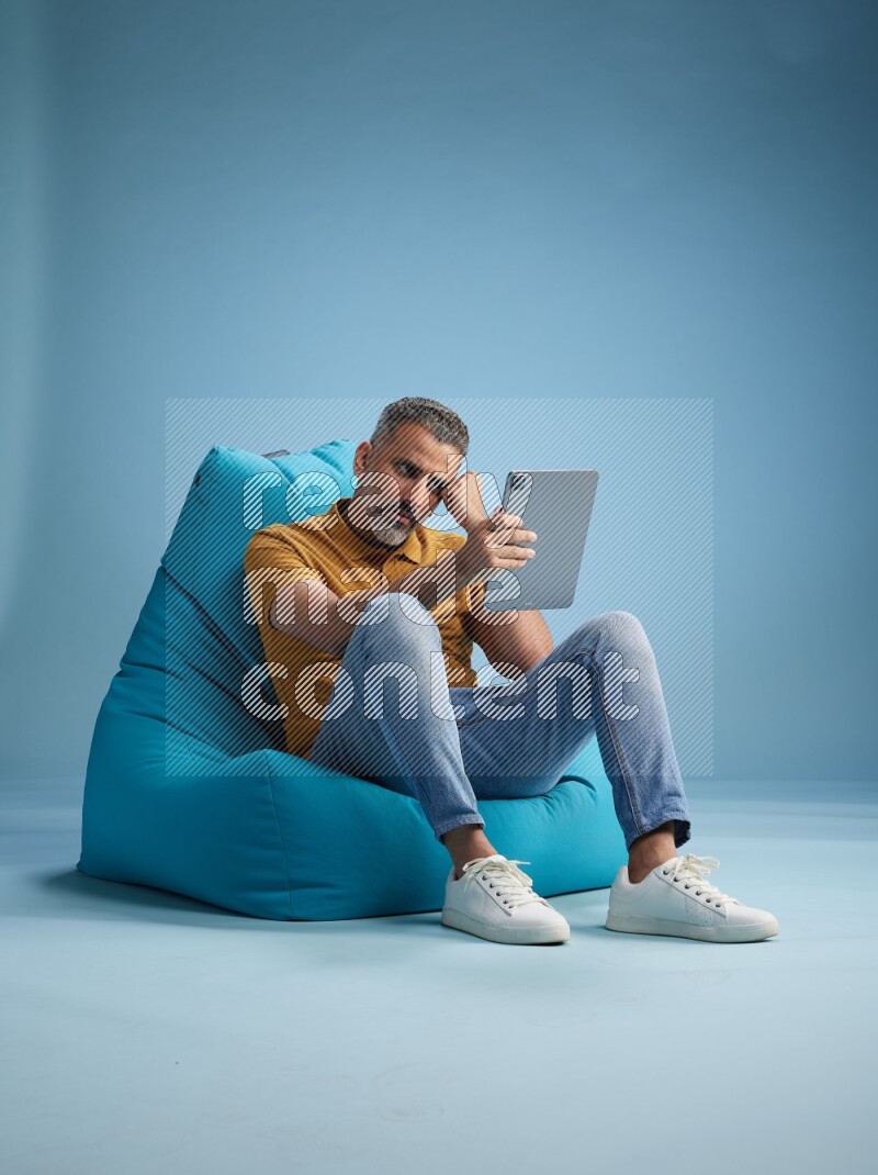 A man sitting on a blue beanbag and working on tablet