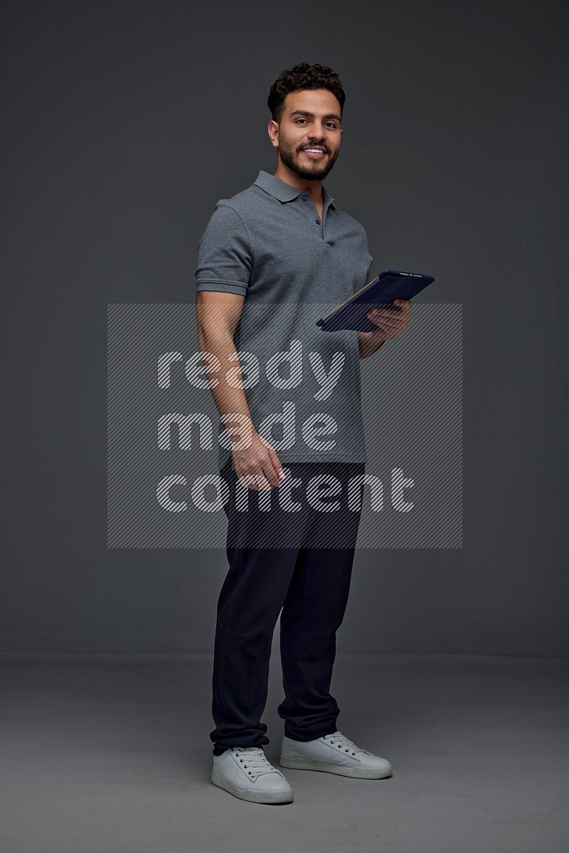 A man wearing casual standing and using his tablet and making multi hand gestures different angles eye level on a gray background